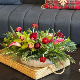 Low floral centerpiece with red blooms, pink calla lilies, and green orchids in a white container