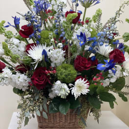 Basket arrangement of red roses, white daisies, and blue flowers