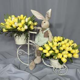 Two yellow tulip arrangements in white buckets with a plush bunny between them