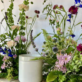 Tall mixed floral arrangement with pink, blue, and green blooms around a white container