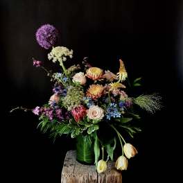 Mixed floral arrangement with roses, tulips, and purple allium in a green vase