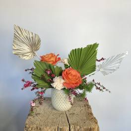 Orange roses in a white textured vase with fan-shaped leaves and metallic accents