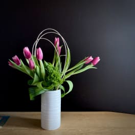 Pink tulips arranged in a white vase with curved wire accents
