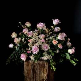 Pink roses and small filler flowers arranged on a rustic wood base