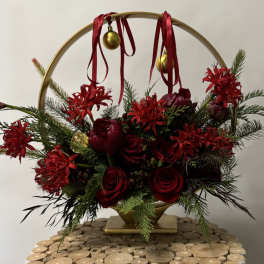 Red roses and holiday flowers arranged in a gold hoop with ribbon and ornaments