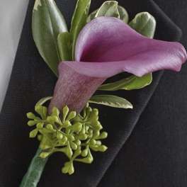 Purple calla lily boutonniere with green accents on a dark suit lapel