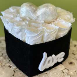 White roses in a black heart-shaped box with a silver heart topper