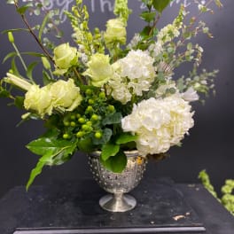 Green and white floral arrangement in a silver urn vase