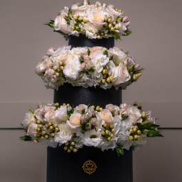Three-tier floral arrangement of white and blush roses in a black box