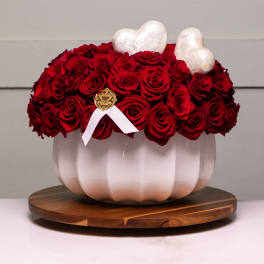 Red rose arrangement in a white pumpkin-shaped vase with heart accents