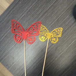 Two butterfly-shaped decorative picks on sticks, one red and one yellow