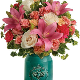 Pink lilies and roses arranged in a teal vase with a bee design