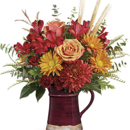 Autumn bouquet of red and orange flowers in a burgundy pitcher vase