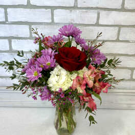 Mixed bouquet of red, pink, purple, and white flowers in a clear glass vase