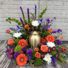 Colorful floral urn arrangement with orange roses, gerberas, and purple blooms