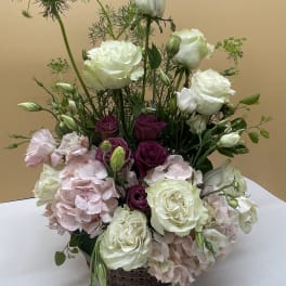 Tall floral arrangement with white roses, pink hydrangeas, and purple blooms in a basket