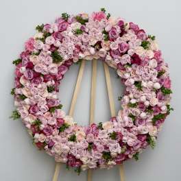 Circular floral wreath of pink and lavender roses on a wooden stand