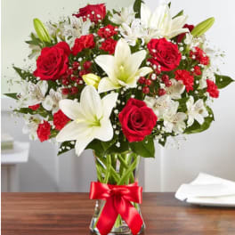 Red roses and white lilies in a glass vase with a red ribbon