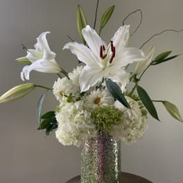 White lilies and white blooms arranged in a tall silver vase