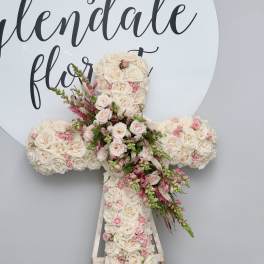 Cross-shaped floral arrangement of cream and pink roses on an easel