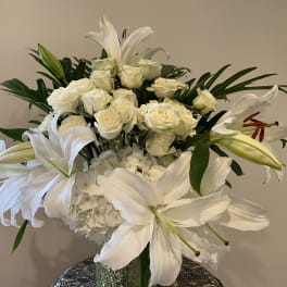 White roses and lilies arranged in a vase with green foliage