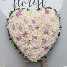 Heart-shaped floral arrangement of white and pink roses on an easel