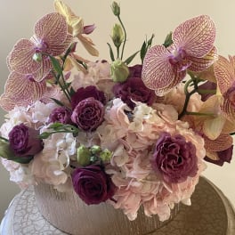 Pink and purple floral arrangement with orchids and hydrangeas in a textured vase