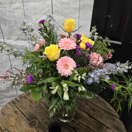 Mixed bouquet with yellow roses, pink gerbera daisies, and purple flowers in a glass vase