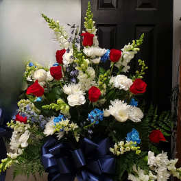 Large floral arrangement with red roses, white blooms, and blue accents in a white vase