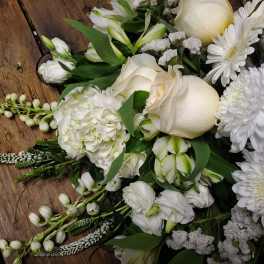 White floral arrangement with roses, daisies, and lilies on a wooden surface