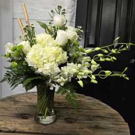 White floral arrangement in a clear glass vase with orchids and roses