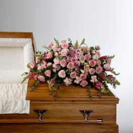 Pink rose and lily casket spray displayed on a wooden casket with white interior lining