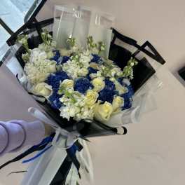 Bouquet of white roses and blue hydrangeas wrapped in black and clear paper