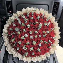 Large bouquet of red roses wrapped in beige paper with eucalyptus accents