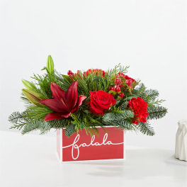 Red floral arrangement in a red gift box with evergreen accents