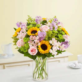 Mixed bouquet of sunflowers, pink roses, and lilac flowers in a glass vase