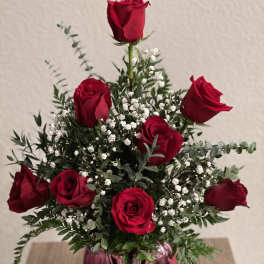 Red roses arranged in a pink glass vase with white filler flowers