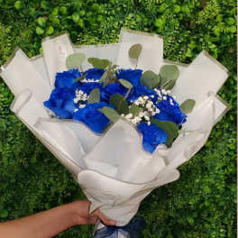 Handheld bouquet of vivid blue roses and white filler flowers wrapped in white paper