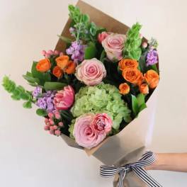 Hand-tied bouquet of pink, orange, and purple flowers wrapped in paper
