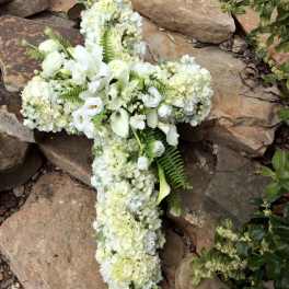 White floral cross arrangement on rocks with calla lilies and hydrangeas