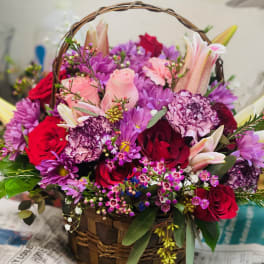 Basket arrangement of pink, red, and purple flowers with lilies and roses