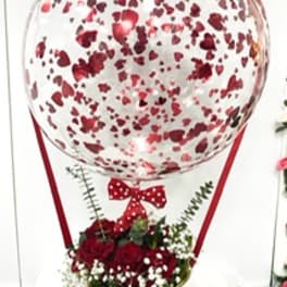 Heart-patterned balloon above a red rose arrangement in a gold vase