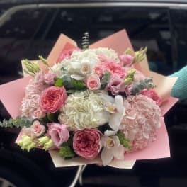 Pink and white bouquet with roses, hydrangeas, and orchids wrapped in pink paper
