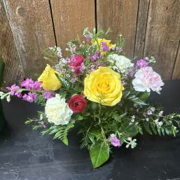 Low mixed arrangement with yellow roses, white and pink carnations, and small pink blooms.