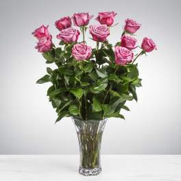 Tall arrangement of pink roses in a clear glass vase on a light surface