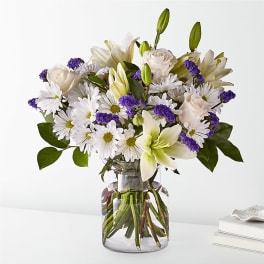 White lilies, roses, and daisies in a clear glass vase