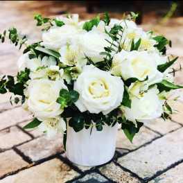 White rose bouquet in a white vase with green foliage