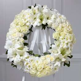 Standing white funeral wreath of lilies, roses, and mums on an easel with white ribbon