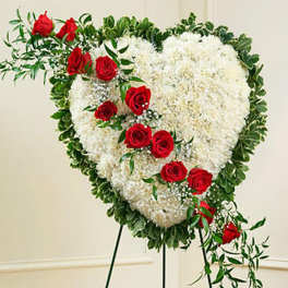 Standing heart-shaped wreath of white flowers with red roses on a metal easel