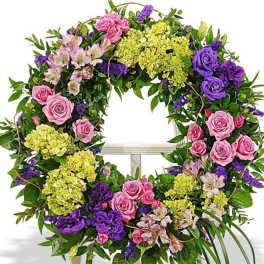 Round wreath of pink roses, purple flowers, and green blooms displayed on a white easel